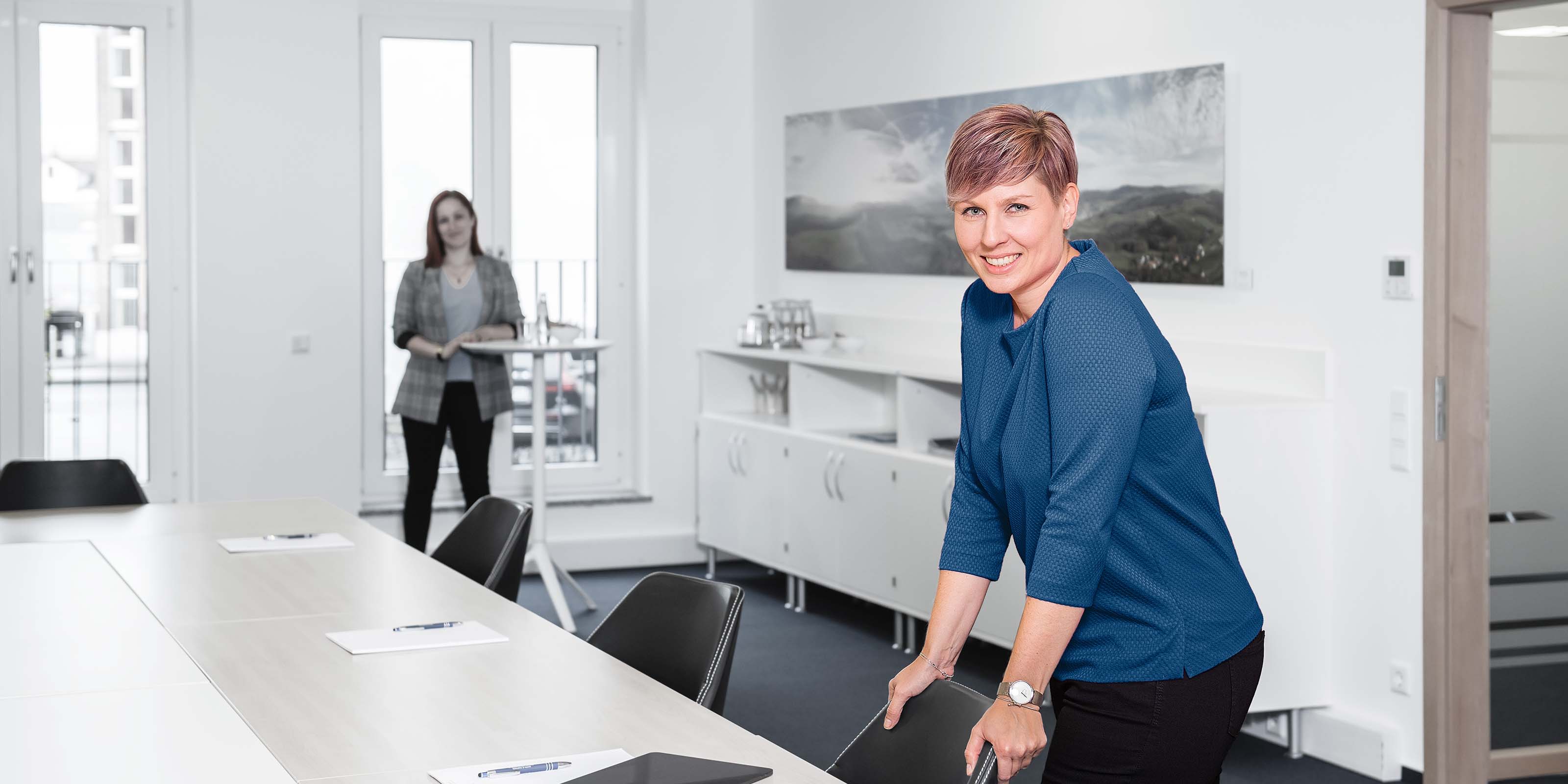 Dame steht bei Konferenztisch und lächelt - 